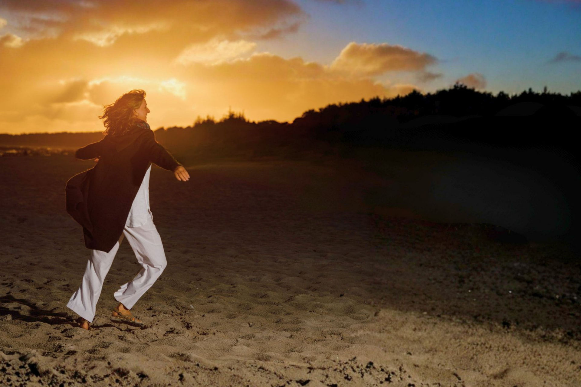 Barbara Rainer geht bei Sonnenuntergang über eine weite Düne am Meer